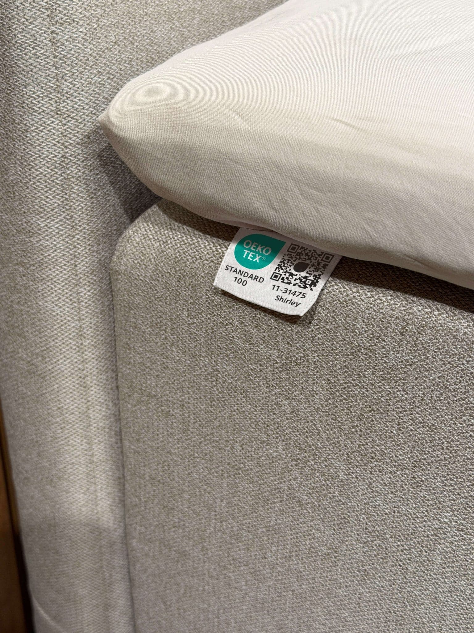 OEKO-TEX® STANDARD 100-label, vastgenaaid aan de beige bekleding van het bed onder het laken