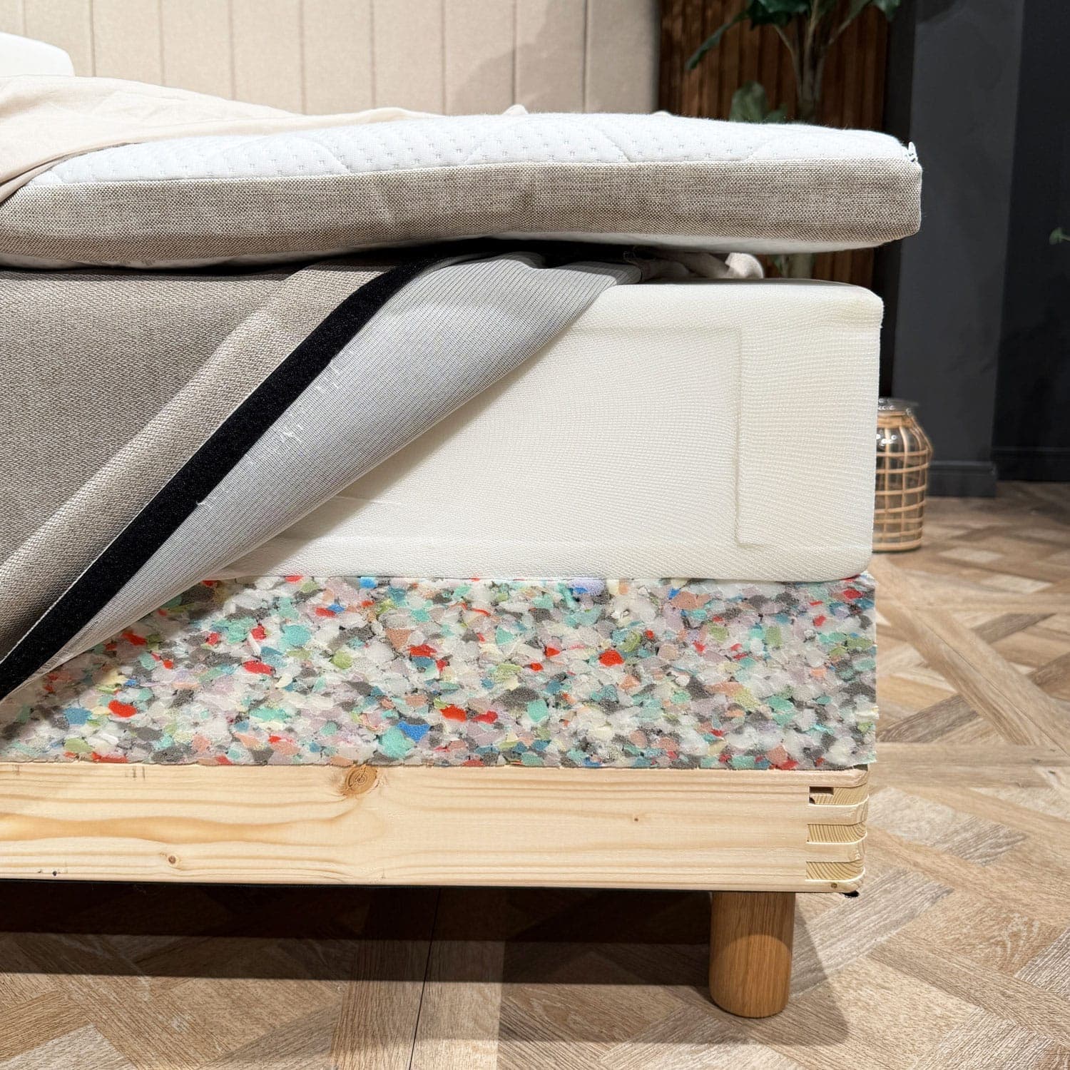 De lagen van het bed zijn bij de hoek geopend: een topmatras, een binnenveringsmatras met geopende hoes en de schuimrand van de bedbodem boven het houten frame