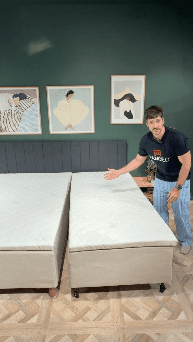Een man toont het uitbreidingsbed op wielen, volledig tegen het bestaande bed aangerold