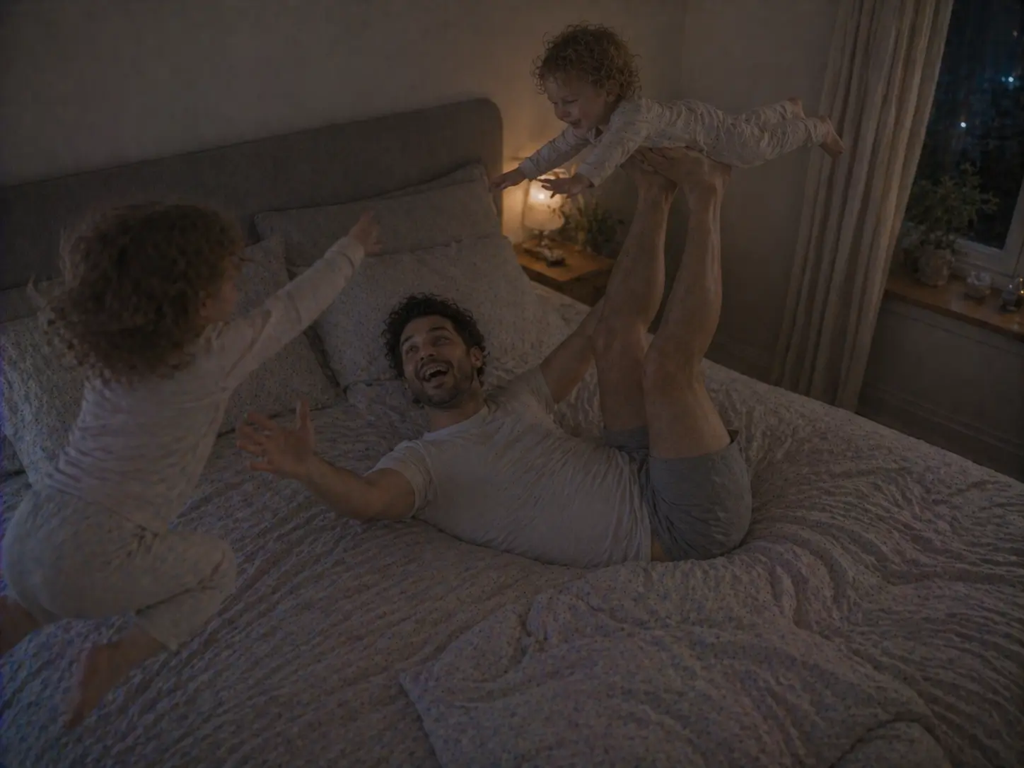 Een vader speelt vliegtuigje met het ene kind op bed, terwijl het andere kind ernaast springt